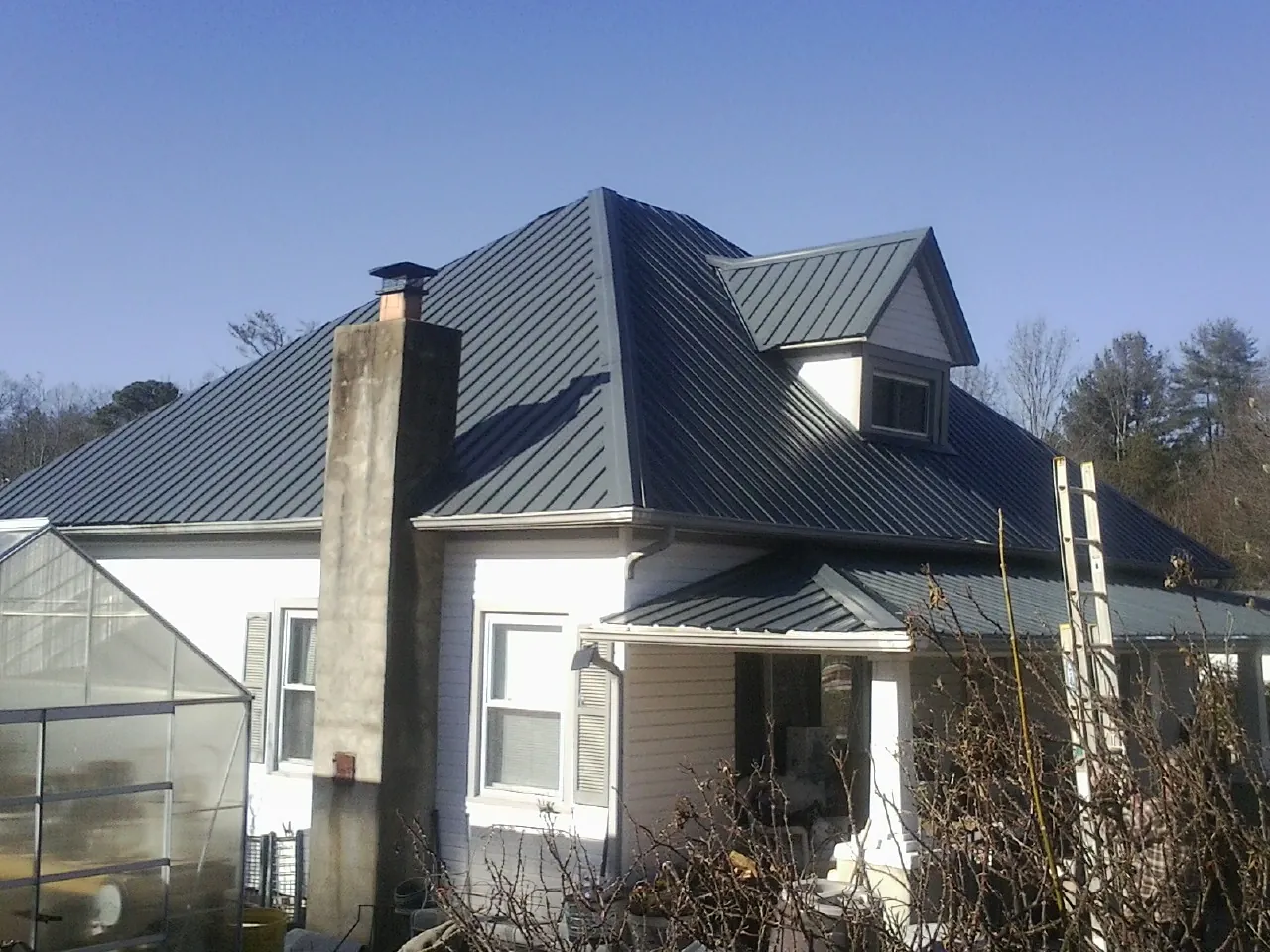 Dark blue standing seam metal roof on a white farmhouse with dormer — Slate & Tile Roof Repair by Roofing Brothers in Elizabeth City