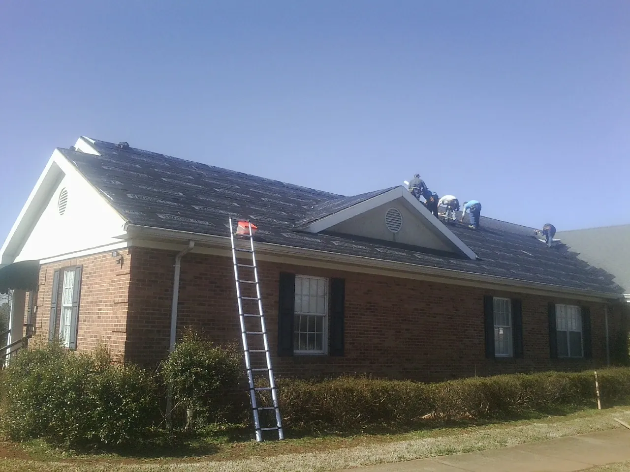 Crew tearing shingles off a brick ranch roof with a ladder set — Emergency Roof Repair work by our crew in Elizabeth City