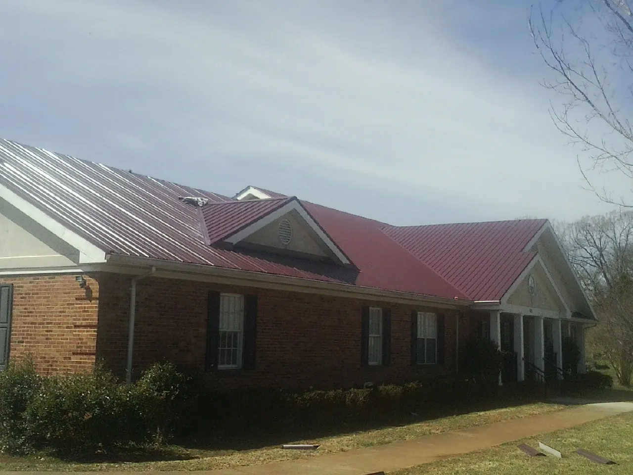 Red metal roof with gabled entries on a long brick building, from a Hail Damage Roof Repair job in Elizabeth City