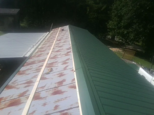 Old rusted panels beside newly installed green metal roofing — Wind Damage Roof Repair by Roofing Brothers in Elizabeth City