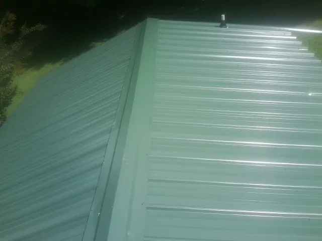 New green metal panels meeting at the ridge of a roof — Flat Roof Repair work by our crew in Elizabeth City