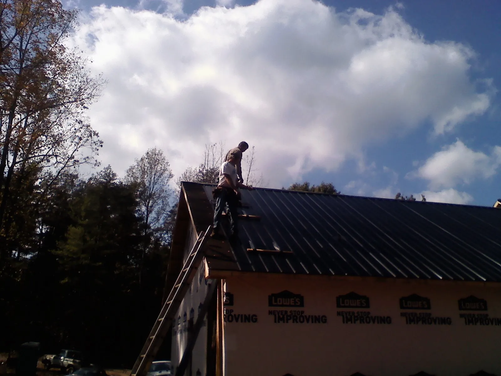 Roofer fastening dark metal panels high against a cloudy sky, from a Roof Inspection job in Elizabeth City