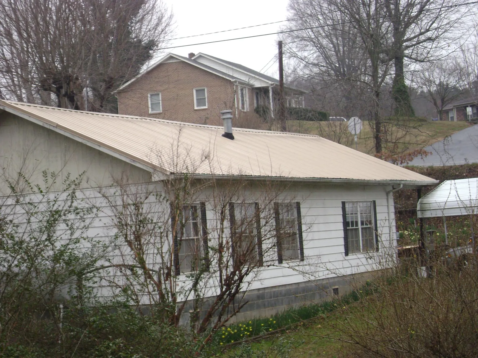 Tan metal roof on a white sided house set into a hillside — Commercial Roofing by Roofing Brothers in Elizabeth City